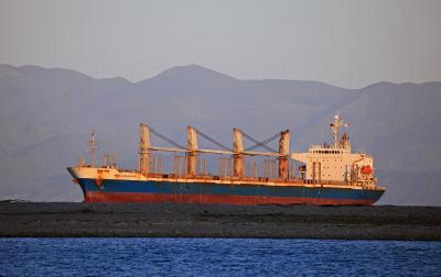 a bulk carrier ship in calm waters in rising or setting sunlight, mountaint in the background