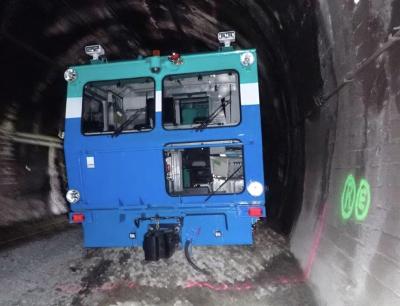 Font-end view of the tamper machine. Railway tracks are nowhere to be seen as it has run over the end of the tracks. The tamper's front wheels are out of sight, buried in the gravel ballast. Its front w