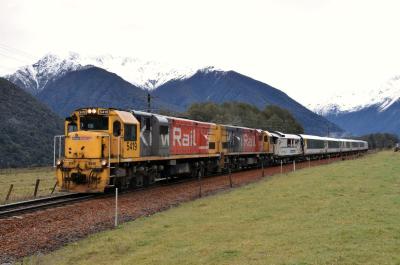 TranzAlpine train - two locomotives and several carriages in a rural setting with snow-capped mountains in the background