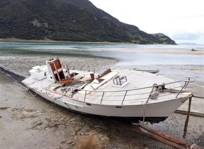 On a estuary beach sits the salvaged hull and main deck of the fishing vessel wreck. Almost all superstructure is missing. 