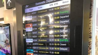 A large VDU screen at a NZ airport displays a list of flights, all delayed. 