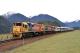 TranzAlpine train - two locomotives and several carriages in a rural setting with snow-capped mountains in the background