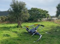 The accident helicopter wrecked at the accident site, a paddock adjoining the Arapito River. Photo: NZ Police The accident - wreckage. image depicts the helicopter wreck in a paddock beside the Arapito River. the fuselage is largely intact but bent in several places. the tail boom appears broken in several places, as do the main rotor blades, which ar still attached to the main rotor hub