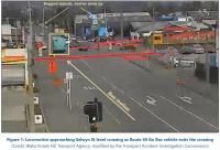 Fig1 from report. still image from CCTV, depicting the incident. An urban low-level light industrail area. Selwyn street is in the centre of the view from foreground to distance. The level crossing is in the middle. A bus has clearly just crossed the level crossing, travelling away from the camera view. A locomotive approaches the bus, approximately twelve metres away