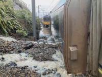 The accident scene. TAIC photo photo of accident scene. water rushes across landslip debris on to rail tracks. Carriages stand upright in the debris.