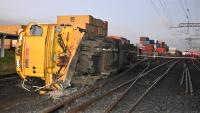 The locomotive, DC4605 lies on its side at the accident site | Photo credit Darren Masters via NZ Herald A rail locomotive lies on its side beside a set of railway points. Railway power lines are overhead, intact. In the distance are shipping containers stacked in land adjoining the rail corridor.