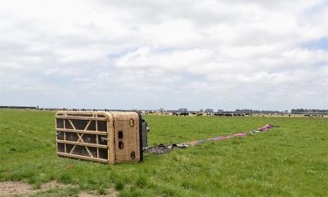 Photo depicts the accident scene. The basket that held the occupants lies on its side in a paddock. The deflated balloon envelope lies stretched out and folded. 