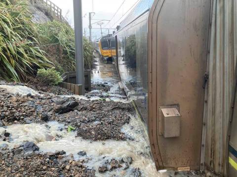 Photo taken close-up along length of train embedded in landslip debris and flowing water
